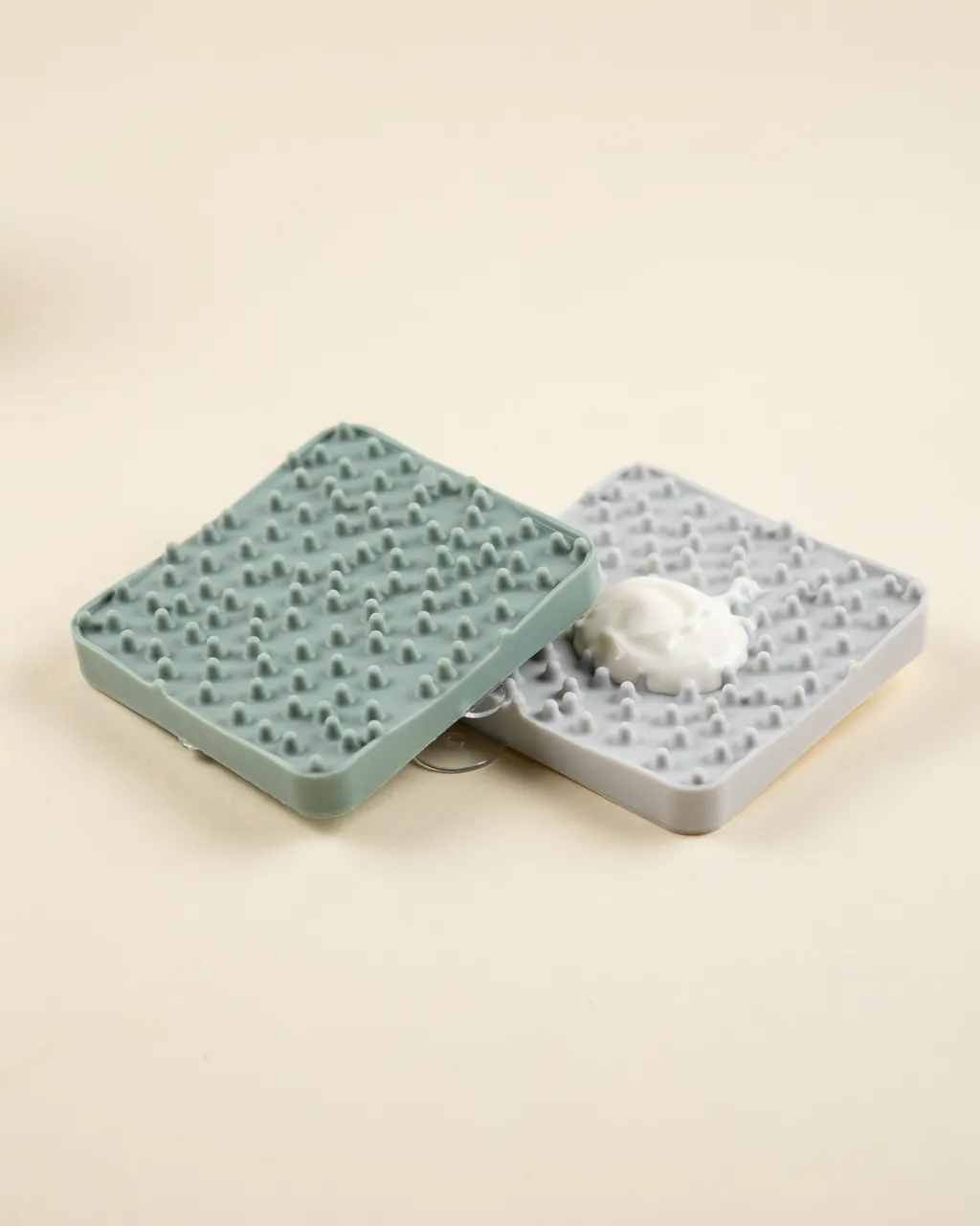 Deux tapis de léchage carrés en silicone, vert sauge et gris, l’un garni de yaourt
