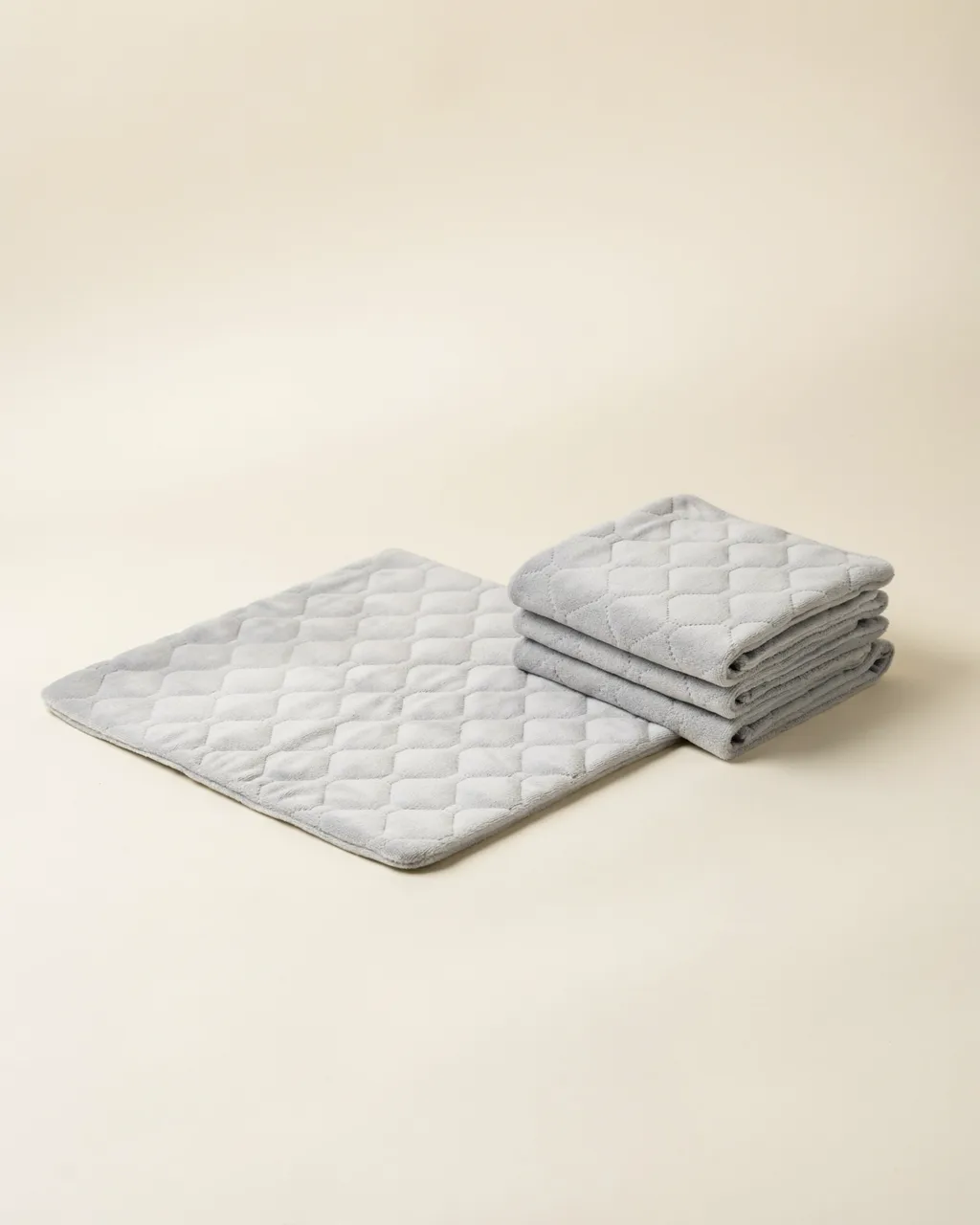 Alèse lavable gris clair au tissu doux matelassé, dépliée à côté de trois alèses pliées